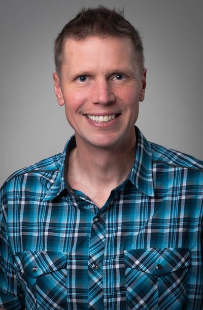 Smiling man in a plaid shirt against a neutral background