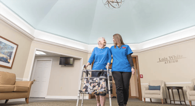 A caregiver assists a resident in an indoor atrium space