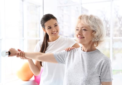 Resident exercising with staff assistance in a bright room
