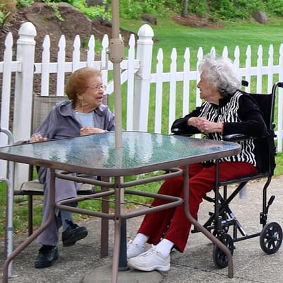 Two elderly women chatting at an outdoor table
