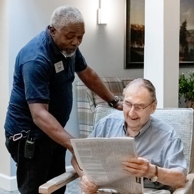 Resident smiling while reading a newspaper with staff assistance