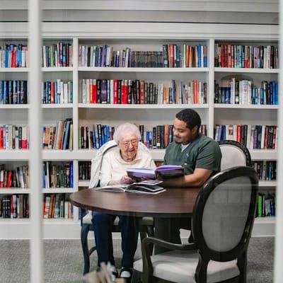 Resident and staff member reading together in a library