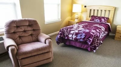 Cozy resident room with bed and chair.