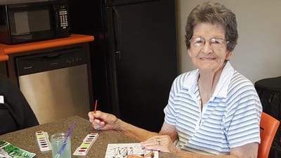 Senior resident painting at a table.
