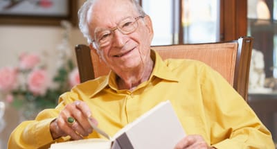 Senior man reading a book indoors, smiling.