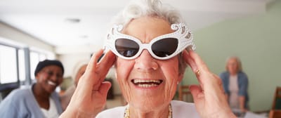 Elderly woman smiling with sunglasses in a community space.