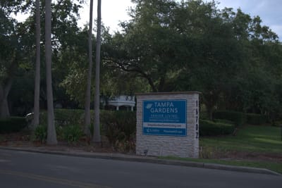 Sign for Tampa Gardens Senior Living visible among trees