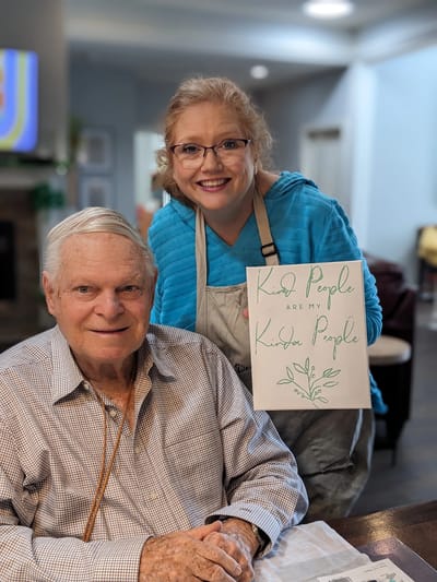 Resident and staff member smiling with sign.