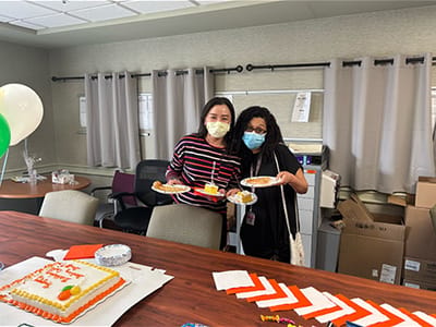Two staff members celebrating with food and a cake.