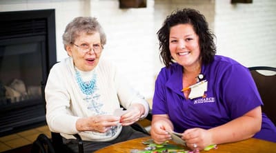 Senior resident and staff member playing cards together.