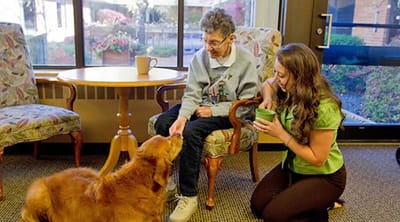 The Estates at Twin Rivers, Nursing Home in Anoka, MN — Senior resident interacting with a therapy dog and caregiver