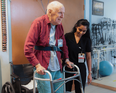 Resident assisted by staff in a rehabilitation setting.