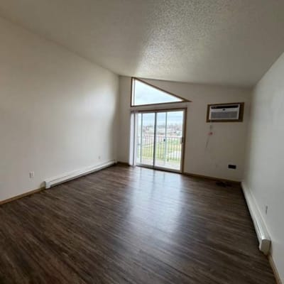 Empty room with large windows and wooden floors.