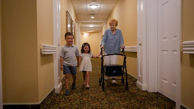 A senior resident walking with children in a hallway