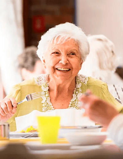 Smiling elderly woman enjoying a meal in the dining room.