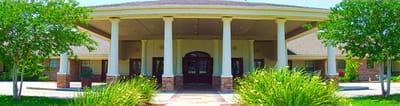 Entrance of a senior living facility with columns and landscaping.