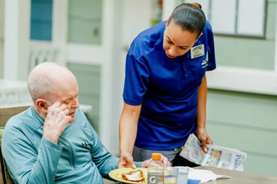 Staff serving food to a resident in the dining area.