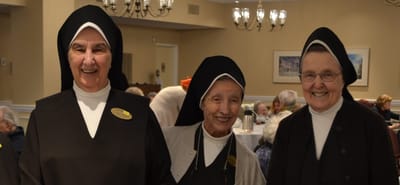 Three smiling nuns in a common area of the facility.