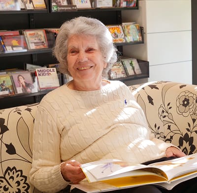 Senior resident reading in a cozy common area.