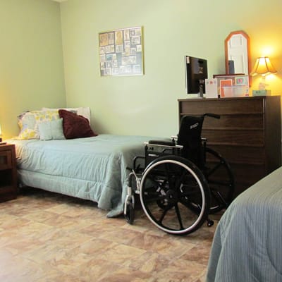 A cozy resident room with two beds and a wheelchair