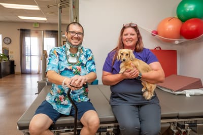 A staff member with a resident and a dog in an activity room