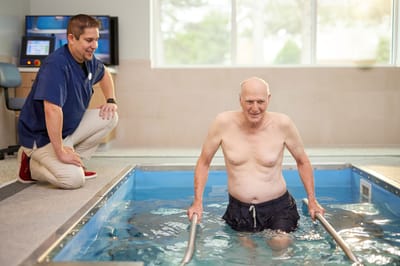 A resident participating in aquatic therapy with staff assistance