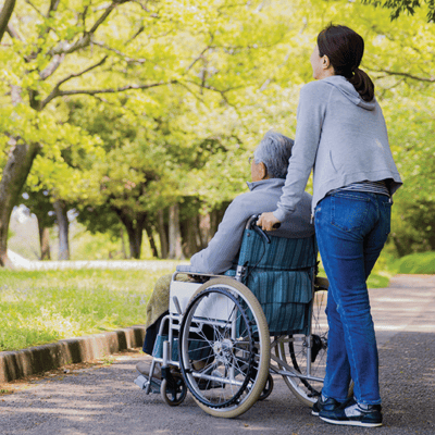 A caregiver pushing a resident in a wheelchair through a park