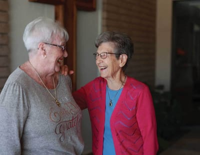 Two residents smiling and enjoying a conversation in the facility