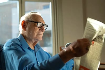 An elderly man reading a newspaper in a sunlit room