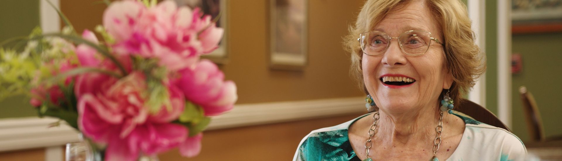 Smiling resident with flowers at a dining table