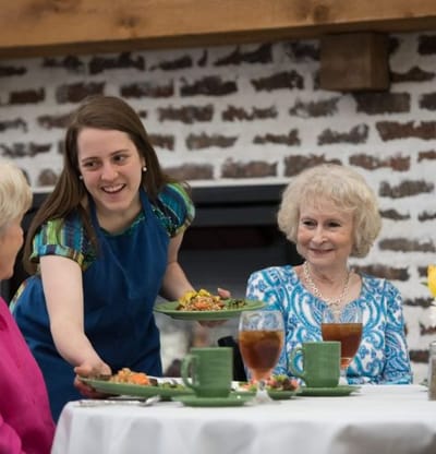Server serving food to residents in a dining room