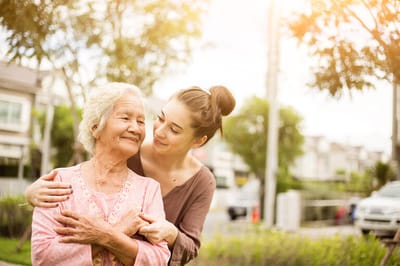 A caregiver and a happy senior woman embracing in a garden