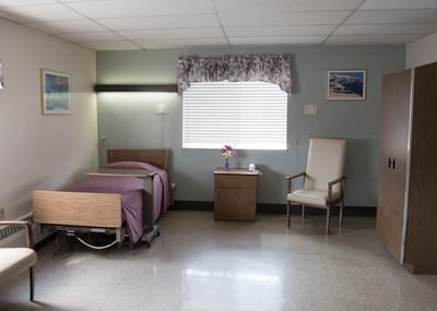 A private room with a bed and chair in a nursing facility