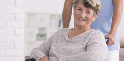 Smiling resident in a wheelchair with staff member behind
