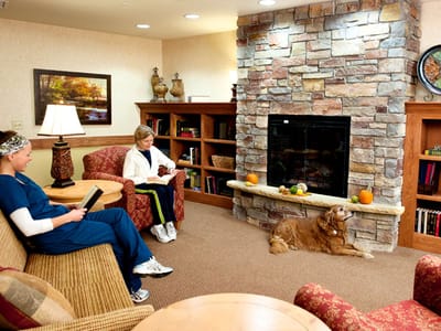 Residents reading in a cozy common area with a fireplace
