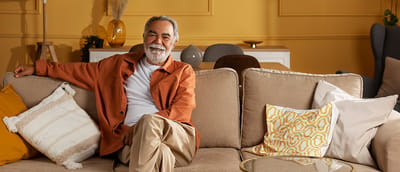 A smiling senior man sitting on a couch in a cozy living area