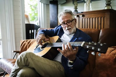 An elderly man playing guitar in a cozy indoor setting