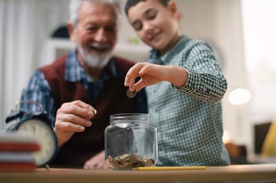 A senior man and a boy adding coins to a jar
