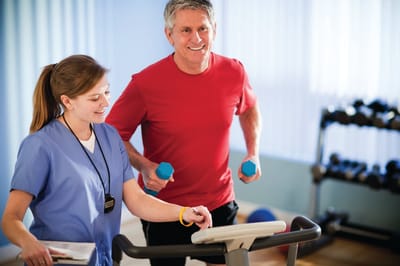 Senior man exercising with staff assistance indoors.