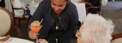 Staff serving a cocktail to a resident in a dining area.