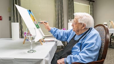 An elder woman painting in a bright activity room