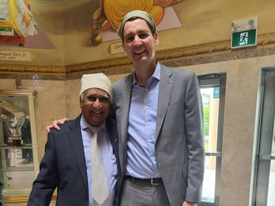Two men smiling together indoors, wearing head coverings
