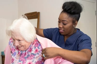 A staff member assisting a resident with a pink jacket