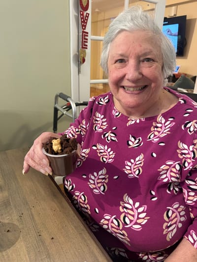 Smiling resident holding a dessert cup in dining area