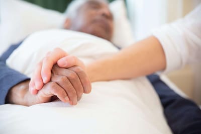 Caregiver holding hands with a resident in bed