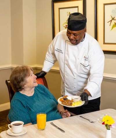 Chef serving a meal to a resident in the dining area