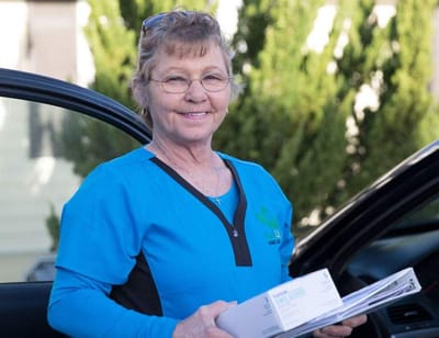 A staff member smiling with paperwork by a vehicle