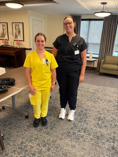 Two staff members in scrubs smiling indoors.