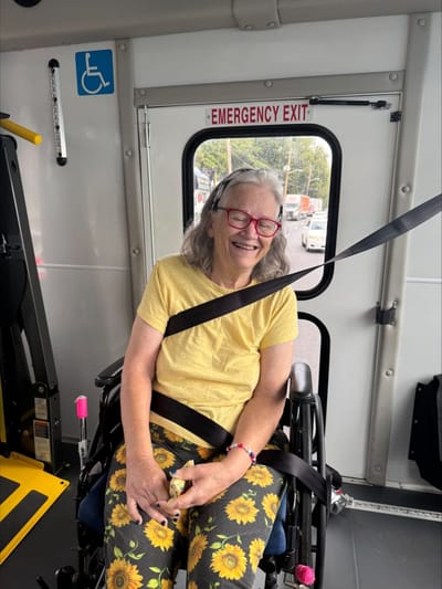 Elderly woman in a wheelchair smiling inside a transport van.
