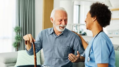 Elderly man and caregiver smiling and interacting in an interior setting.